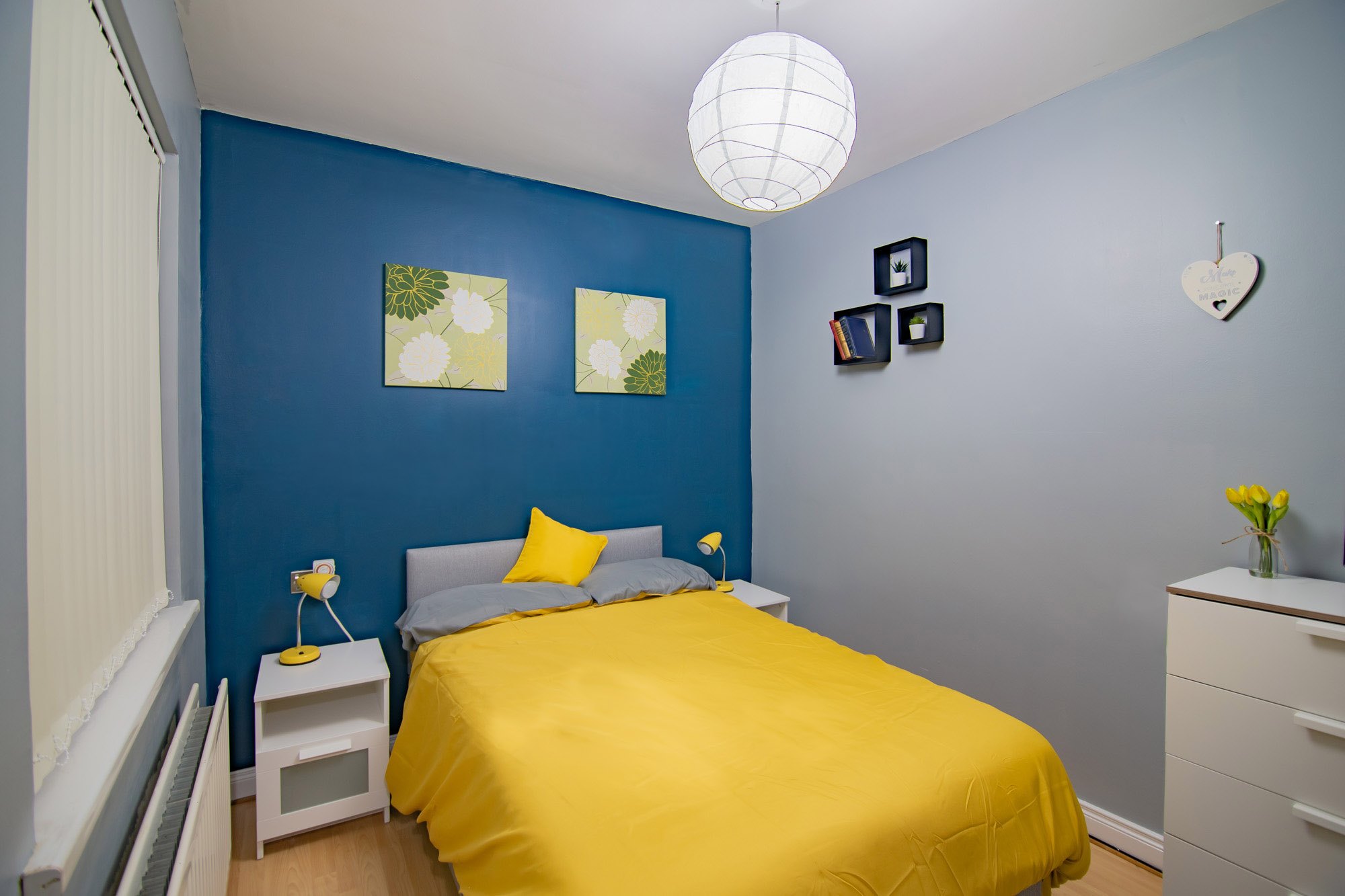 Furnished double bedroom with blue feature wall and yellow bedding at The Mount